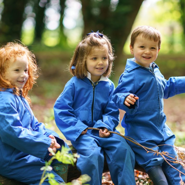 3 children sat down wearing blue overalls