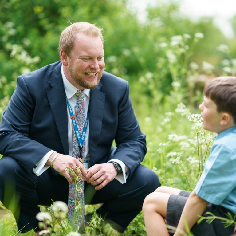 student sat in overgrown grass with his teacher