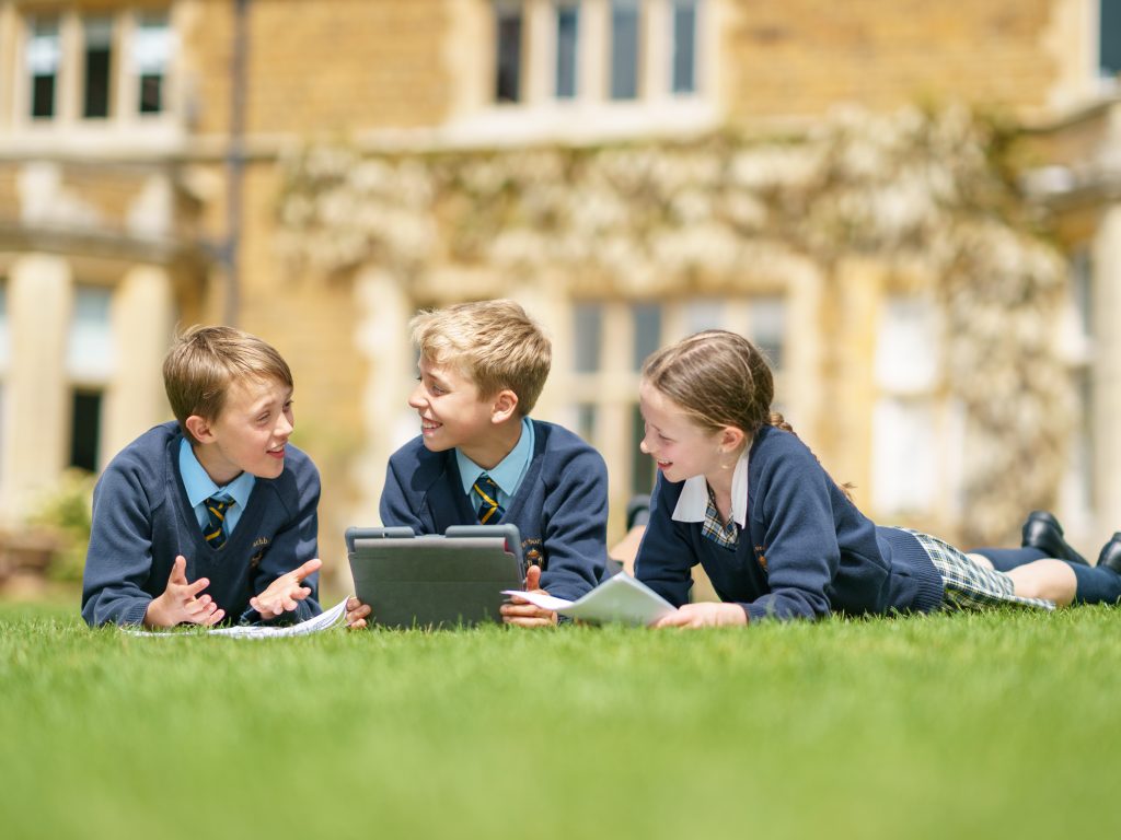 3 students laid down in the grass working together