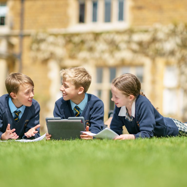 3 students laid down in the grass working together