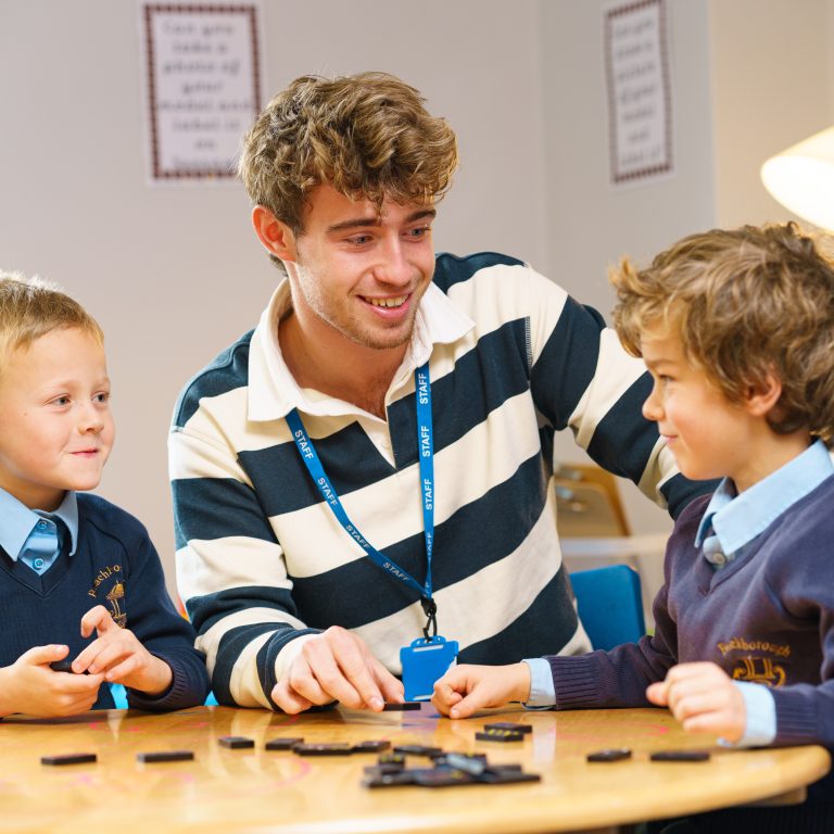 teacher helping 2 students play dominoes