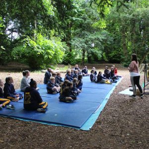 students sat on mats in the forest, with a teacher talking to them