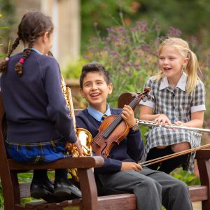 children sat on a bench holding musical instruments