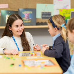 Teacher talking to pupil in classroom whilst learning maths