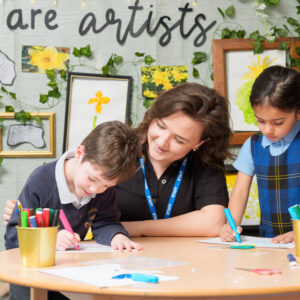 Early Years teacher with two children looking at their work in classroom area